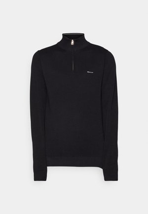 Black knit pullover with a quarter zip, featuring a high collar and ribbed cuffs. The front displays a small logo on the left chest.