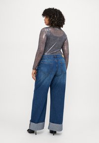 Chemisier à manches longues en voile avec un motif léopard et une texture légère, associé à un jean en denim bleu à jambes larges avec des ourlets retroussés.