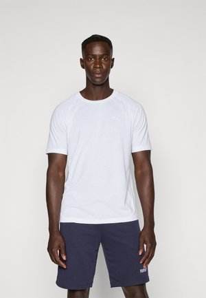White short-sleeve athletic shirt features a round neckline and raglan sleeves. Paired with navy shorts, showcasing a logo detail.