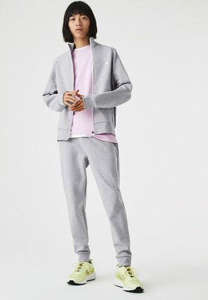 Sudadera gris con cremallera y mangas largas sobre una camiseta rosa claro y joggers grises, combinada con zapatillas deportivas amarillas neón.