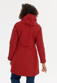 Punainen vedenpitävä takki hupulla, vyötämyksellä ja pitkillä hihoilla. Ominaisuuksiin kuuluu korkea kaulus ja napitettavat hihansuut varma sulje.