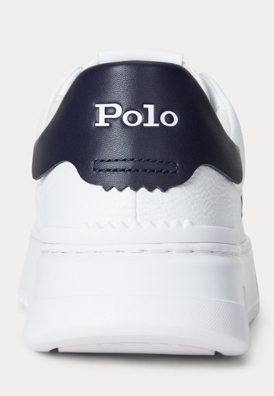 Balts sporta apavs ar tumši zilu papēža siksniņu ar uzrakstu "Polo" baltā krāsā, redzama šuve un reljefa zolīte, skatīts no aizmugures.