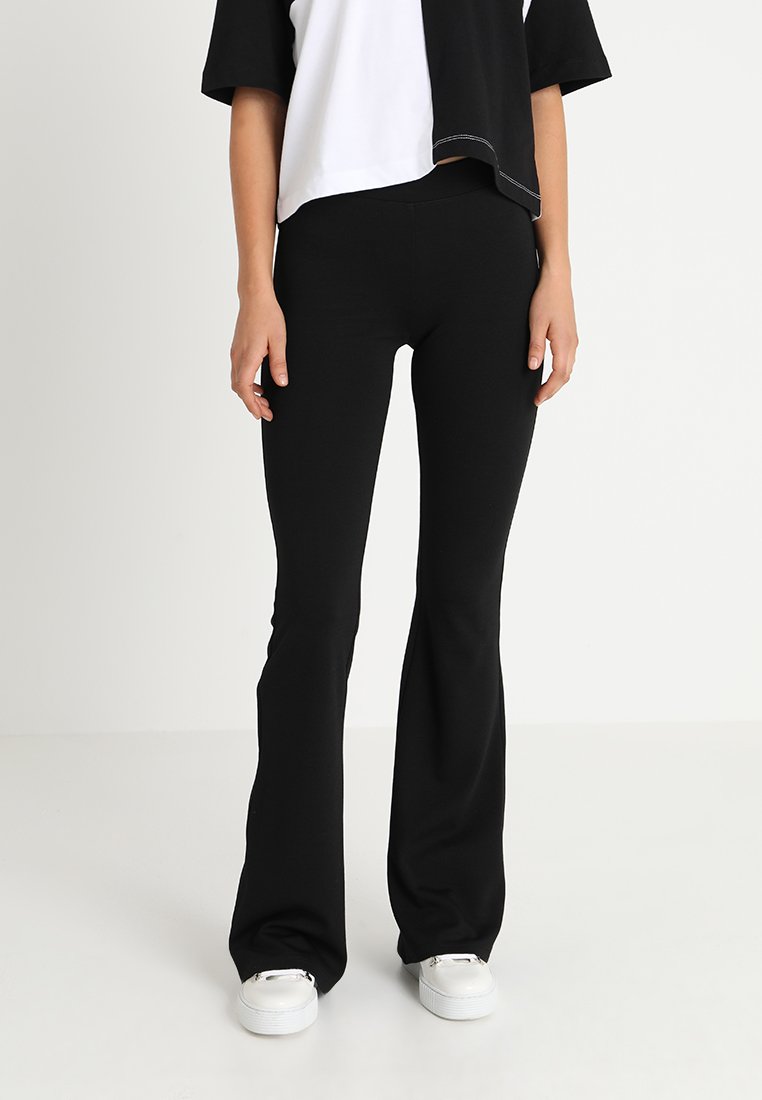 Pantalons noirs évasés en matière douce et extensible. Ajustés au niveau des hanches, ils s'évasent au genou. Texture lisse, détails minimalistes.