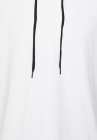 Hvid pullover hættetrøje lavet af blødt stof, med sorte snore og metalspidser, i en afslappet pasform og med et enkelt design.