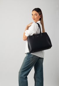 Sac fourre-tout en cuir noir avec une forme structurée, doté de deux poignées et d'accents en métal doré. La texture est lisse avec un minimum de détails.