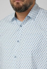 Hellblaues Hemd mit einem Rautenmuster in dunklerem Blau. Kragen mit Knopfverschluss und eine einzelne Brusttasche.