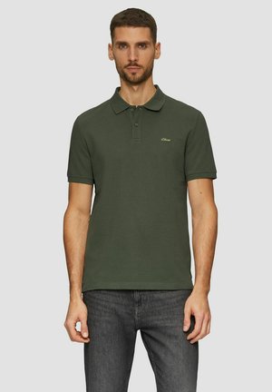 Dunkelgrünes Poloshirt aus Baumwolle mit einem Kragen mit zwei Knöpfen und kurzen Ärmeln. Verfügt über ein kleines goldenes Logo auf der Brust. Getragen mit einer dunklen Jeans.