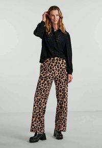 Svart langermet bluse med nagle detaljer, kombinert med vide bukser i leopardmønster og kraftige svarte platåsko.