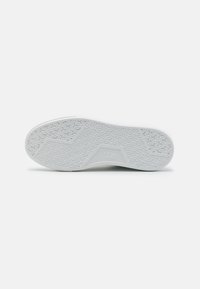 Suela de goma blanca con un patrón texturizado, que presenta un logo central y contornos para el agarre. Acabado suave y diseño aerodinámico.