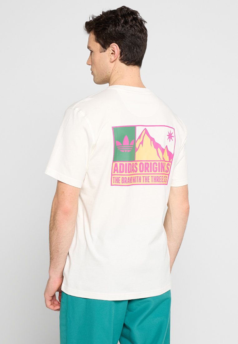 T-shirt bianco in cotone con una stampa grafica colorata sulla schiena con motivi di montagna e stelle, e il testo "ADIDAS ORIGINS" in rosa.