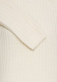 Gestrickter Pullover in Off-White, mit einem strukturierten Stoff, gerippten Bündchen und einem weichen, voluminösen Design. Das Armdetail weist ein breites Strickmuster auf.