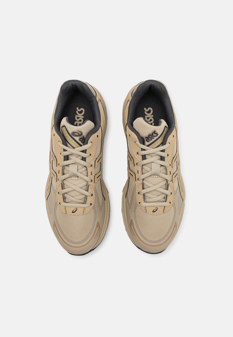 Baskets de sport beiges avec une tige synthétique lisse, un bout arrondi et des détails de couture complexes. Comprend des lacets et un logo de marque.