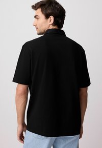 Sort polo shirt med et ensfarvet design, korte ærmer og krave, parret med lyseblå denim jeans. Synlig syning på skjorten.