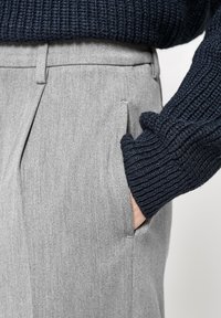 Pantaloni gri, ajustați, cu pliseuri frontale, material texturat și buzunare laterale, asociați cu un pulover tricotat bleumarin, cu manșete din material cu nervuri.