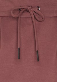 Los pantalones jogger en color burdeos cuentan con una cintura con cordón a juego y puntas metálicas negras, fabricados en una suave tela texturada.