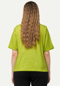 Zelený krátký rukáv top s volným střihem, vyrobený z lehké tkaniny. Má jemnou texturu a zaoblený lem.