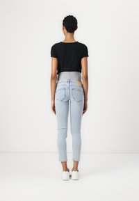 Jeans ajustados de corte slim en color azul claro, con una cinturilla elástica gris, fabricados en denim y con un bolsillo trasero visible. Combinados con una blusa negra de manga corta y canelada.