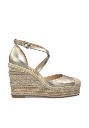 Metaliczne złote espadryle na koturnie z zamkniętym czubkiem, projektem krzyżowych pasków wokół kostki oraz plecioną platformą z juty. Płaska gumowa podeszwa.