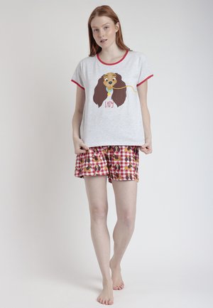 Joven mujer de pie descalza con camiseta gris de manga corta con ilustración de perro y pantalones cortos de cuadros rojos con patrón de perro a juego.