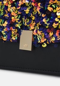 Svart väska med flerfärgade paljetter och ett rektangulärt gyllene spänne med en liten präglad logotyp, närbild.