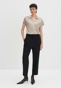 Polo shirt beige a maniche corte abbinato a pantaloni neri su misura. L'outfit è completato da tacchi a punta nera e calze trasparenti alla caviglia.