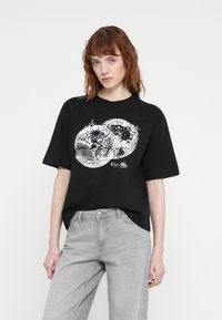 Black oversized t-shirt featuring a silver graphic of two disco balls, with star accents and the text "Disco Fun" beneath them.