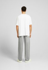 Camiseta de algodón blanca con un corte relajado, combinada con pantalones de mezclilla gris claro. El conjunto presenta un diseño simple y una textura suave.