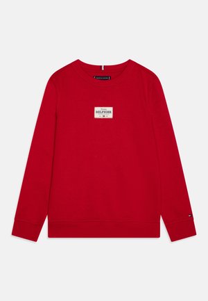 Rød langærmet crewneck sweater med Tommy Hilfiger-logo på brystet centreret og lille logo på venstre håndleds manchet.