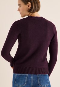 Maglione bordeaux a maniche lunghe con colletto e orlo a coste. Tessuto morbido e design aderente, visto da dietro, abbinato a jeans blu.