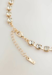 Gold-tone necklace featuring clear crystals in claw settings, with a lobster clasp and adjustable chain extension. Smooth, shiny finish.