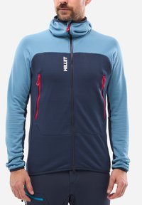 Fleece jacket in light blue and navy, features zippered front pockets and a high collar with red accents. Textured fabric provides warmth.