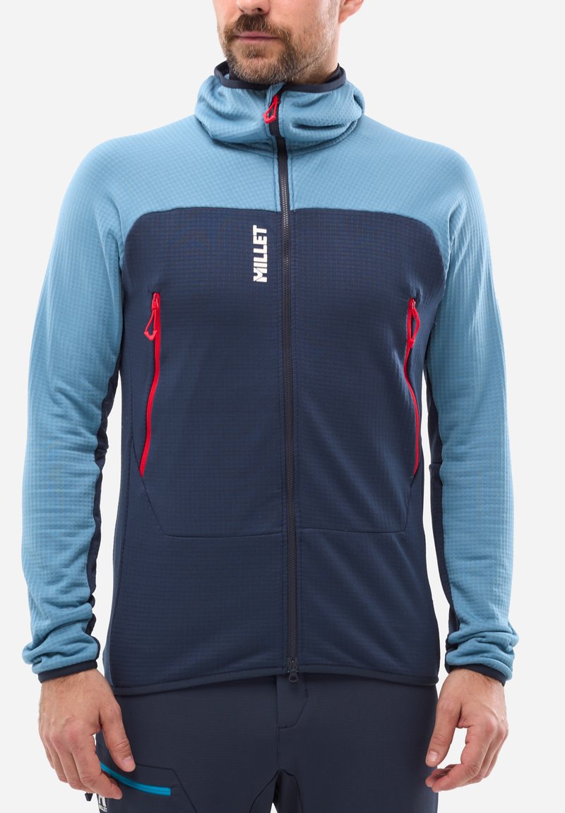 Fleece jacket in light blue and navy, features zippered front pockets and a high collar with red accents. Textured fabric provides warmth.
