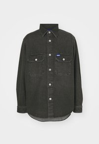 Chemise en denim noire à manches longues avec fermeture par boutons sur le devant, deux poches poitrine à rabats avec boutons, et une petite étiquette de marque bleue sur la poche gauche.