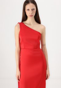 Robe en satin rouge avec un design à une épaule, corsage ajusté et jupe fluide. Texture lisse avec une silhouette épurée et minimaliste.