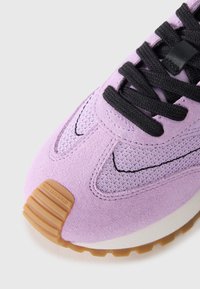 Purple suede sneaker featuring a textured upper, black laces, and rubber outsole. Notable branding on the heel with a beige accent.