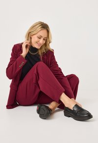 Bordeaux op maat gemaakt pak met een zachte textuur, gecombineerd met zwarte leren instappers met een getextureerde zool en een rode accent op de hak.