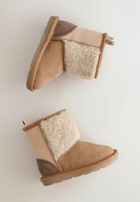 Ein Paar winterliche Stiefel für Kleinkinder in Beige und Tan mit Fleecefutter und strukturierten Gummisohlen auf einem schlichten hellen Hintergrund.