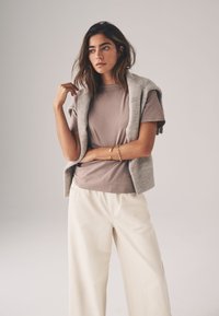 Szary dziergany bezrękawnik noszony na jasnobrązowej koszulce z krótkim rękawem oraz kremowych spodniach o szerokich nogawkach. Skupienie na gładkich fakturach i minimalistycznym designie.