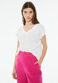 White V-neck T-shirt made of lightweight, slightly sheer fabric, paired with bright pink linen trousers featuring a button closure.