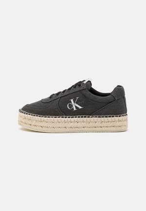 Baskets en toile noires avec un bout rond, semelle en jute de style espadrille surélevée et des détails de logo blancs sur le côté.