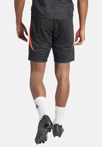 Schwarze Sportshorts mit roten seitlichen Akzenten, aus leichtem Material. Getragen mit weißen Socken und schwarzen Fußballschuhen, die eine enganliegende Passform zeigen.