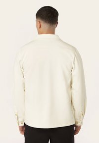 Crème lange mouwen button-up shirt met een rechte snit, voorzien van vierkante schouders, gouden knopen en een gladde textuur.