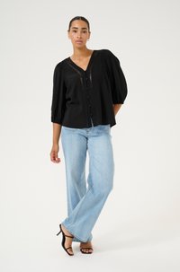 Zwarte, loszittende blouse met pofmouwen, v-hals en knoopsluiting. Draag met lichtblauwe wijde jeans en zwarte strappy hakken.