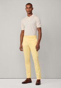 Polo skjorte i lys beige med korte ærmer, kombineret med slim-fit gule bukser og brune loafers. Enkel design og rene linjer.