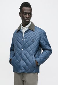 Gesteppte blaue Jacke mit grauem Kragen, Druckknöpfen und Logodetail. Strukturierter Stoff, lange Ärmel und Seitentaschen. Lässiges Design.