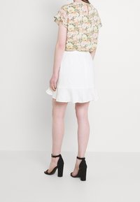 Blusa floral de manga corta, falda acampanada blanca; sandalias de bloque de tacón de ante negro con tiras para el tobillo. Tejido ligero y colores pasteles.