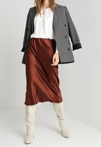 Houndstooth dubbelknäppt blazer i svart och vitt, i kombination med en satinbrun kjol och vita knäskrämmor. Strukturerade tyger och smidig siluett.