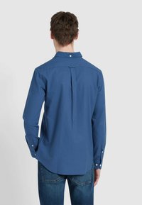 Blauwe langemouwige shirt, met kraag en schouderplooien, knoopsluiting en verstelbare manchetten, gemaakt van een soepele stof. Gecombineerd met denim jeans.