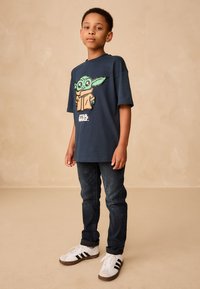 Navy blue T-shirt featuring a cartoon character with green skin and a brown robe, paired with dark jeans and white shoes with black stripes.