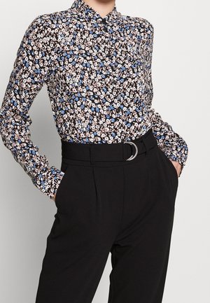 Blomstret bluse med sort baggrund, der har blå og pink mønstre, knaplukning og lange ærmer. Kombinationen med højtaljede sorte bukser.